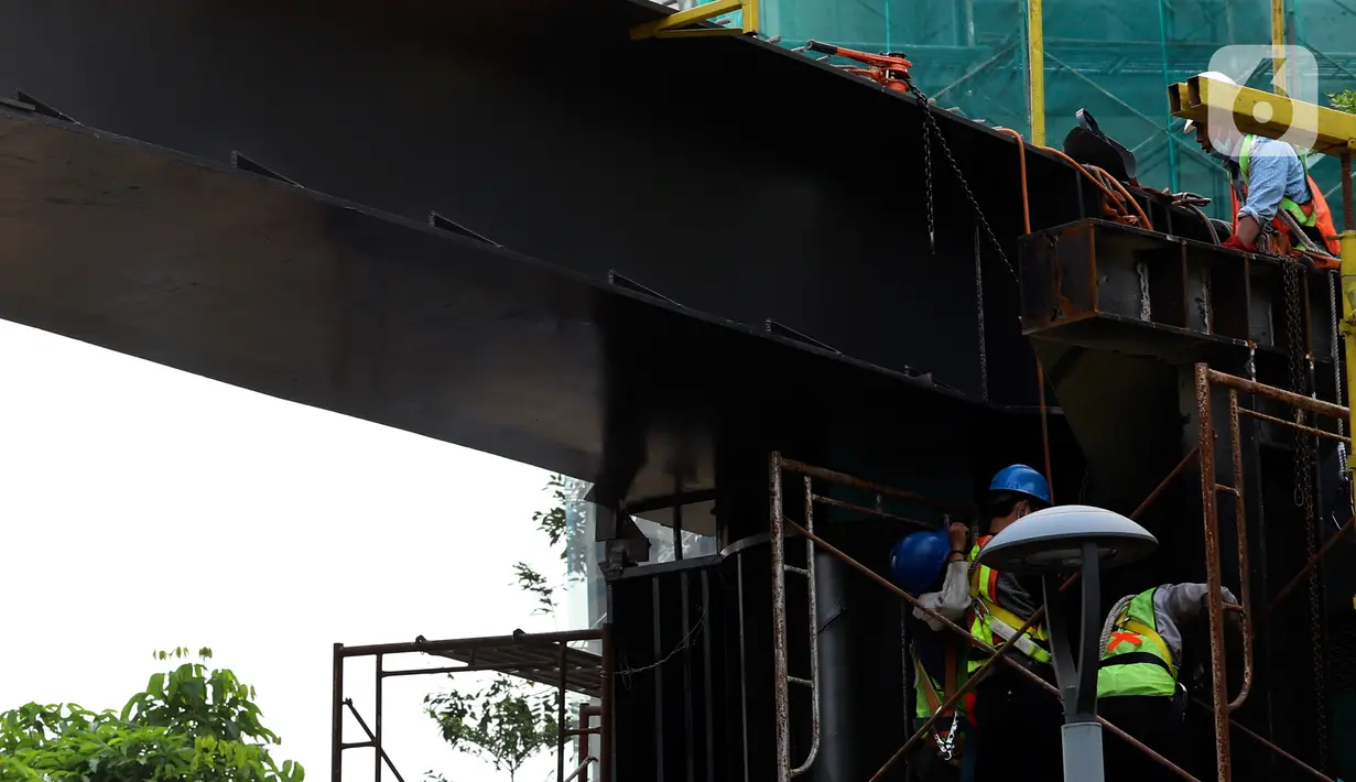 Pekerja menyelesaikan pengerjaan jembatan penyeberangan orang (JPO) dan jembatan penyeberangan sepeda di Karet Sudirman, Jakarta, Jumat (8/10/2021). JPO yang akan dilengkapi jalur sepeda dan terintegrasi dengan halte Transjakarta itu akan rampung pada November 2021. (Liputan6.com/Johan Tallo)