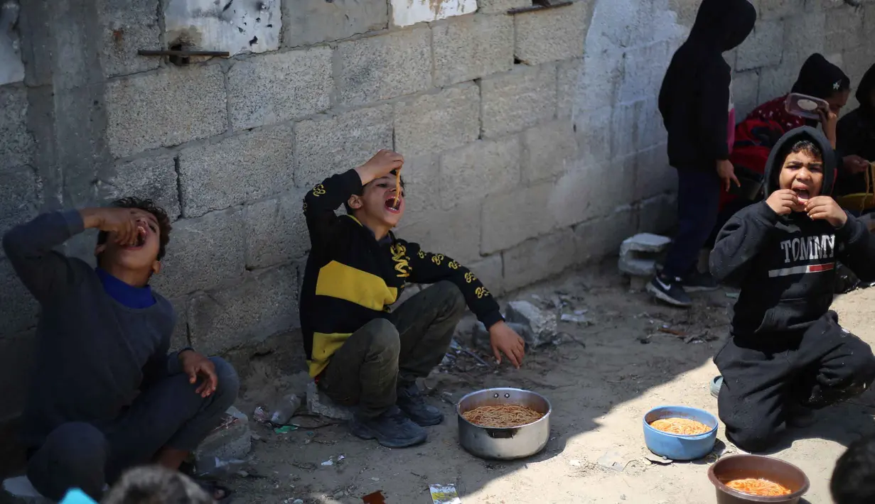 Situasi semakin memburuk ketika sejumlah lembaga bantuan mengurangi distribusi pasokan bahan pangan. World Central Kitchen disebut-sebut menghentikan pasokan tepung harian sebesar 20 hingga 30 ton. Tampak dalam foto, anak-anak pengungsi Palestina memakan makanan yang mereka terima dari dapur amal di kamp pengungsi Nuseirat, Jalur Gaza Tengah pada 13 April 2026. (Eyad Baba/AFP)