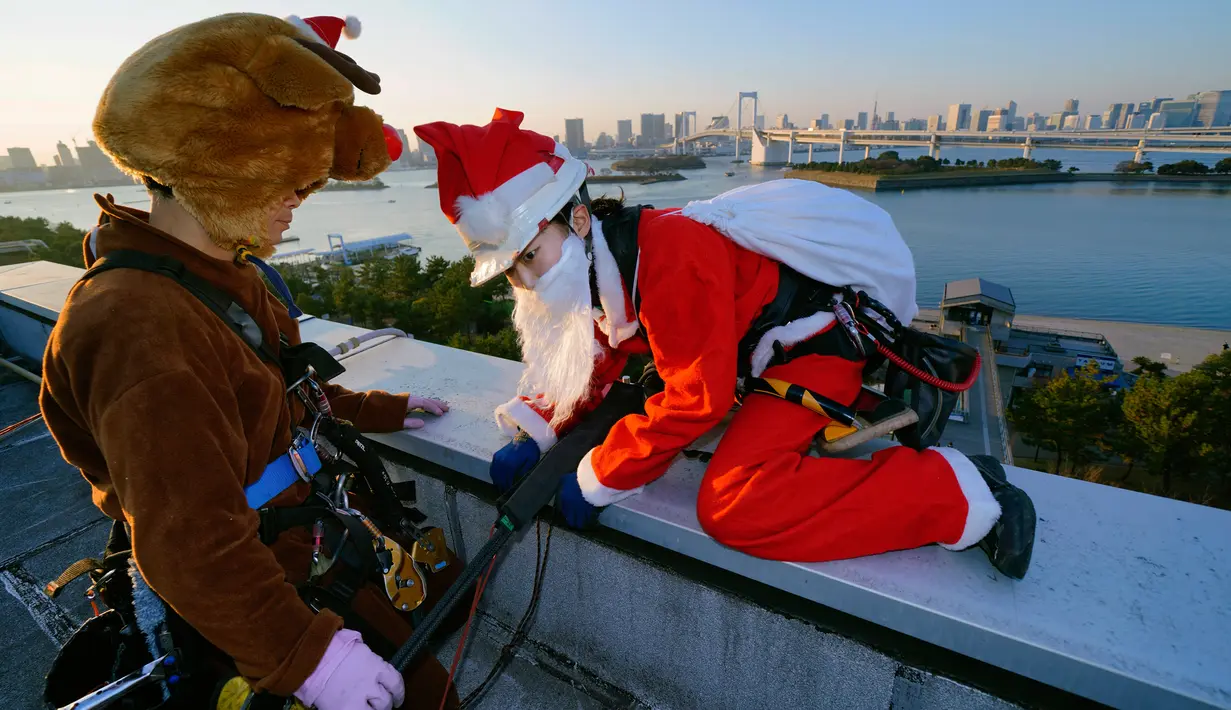 Dua petugas berkostum Santa Claus dan rusa bersiap turun untuk membersihkan kaca-kaca gedung bertingkat di pusat perbelanjaan di Tokyo, Jepang, Kamis (21/12). Para pekerja ini berbagi kecerian Natal dalam bentuk yang berbeda. (AP/Shizuo Kambayashi)