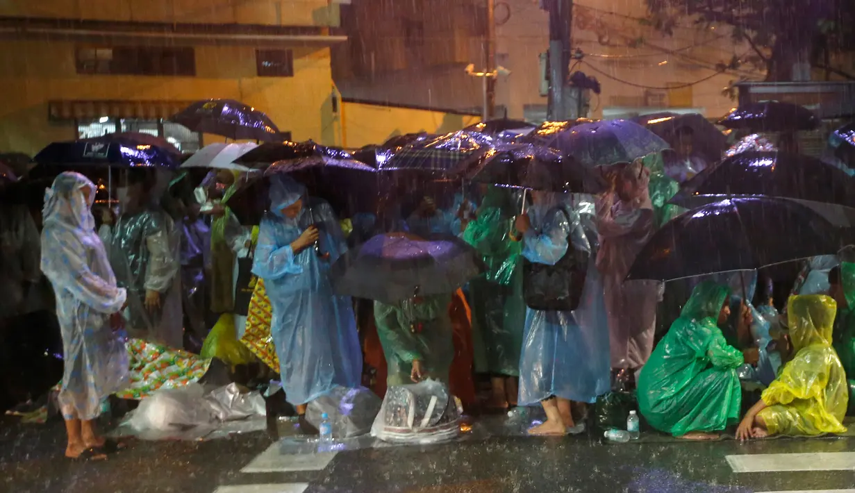 Sejumlah orang memakai jas hujan dan memegang payung demi menghadiri upacara kremasi Raja Thailand Bhumibol Adulyadej di Bangkok, Selasa (24/10). Upacara pemakaman sendiri akan berlangsung selama lima hari mulai Kamis, 26 Oktober 2017. (AP/Sakchai Lalit)