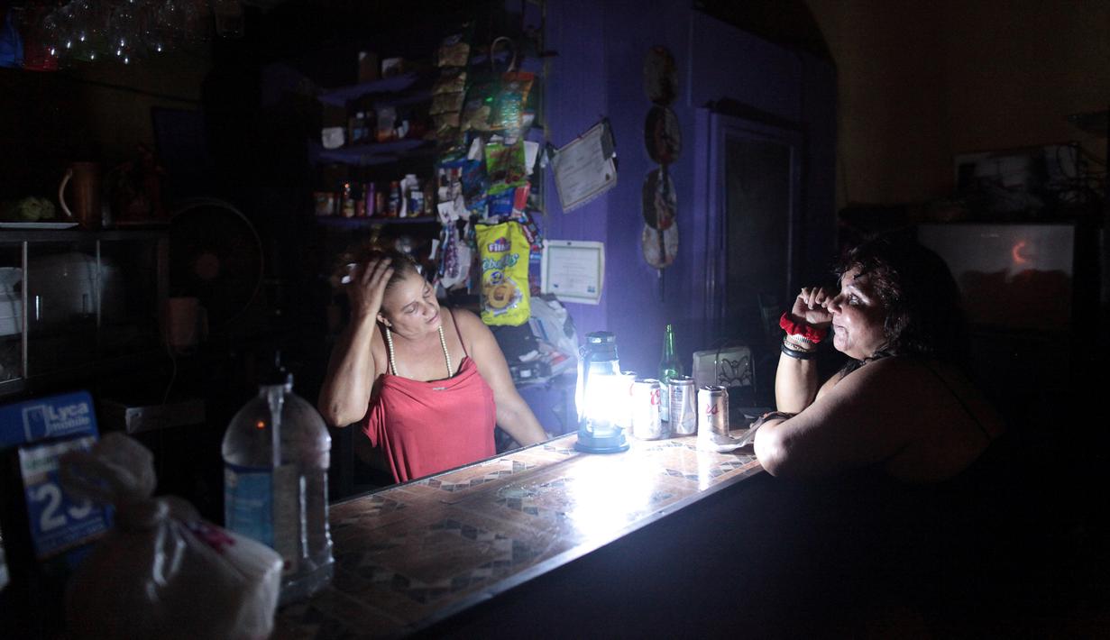 Dua orang wanita berbincang di sebuah kedai kopi selama pemadaman listrik di San Juan, Puerto Rico, Rabu (21/9). Kebakaran yang terjadi di pembangkit listrik Puerto Rico menyebabkan 1,5 juta penduduk pulau itu hidup tanpa listrik. (REUTERS/Alvin Baez)