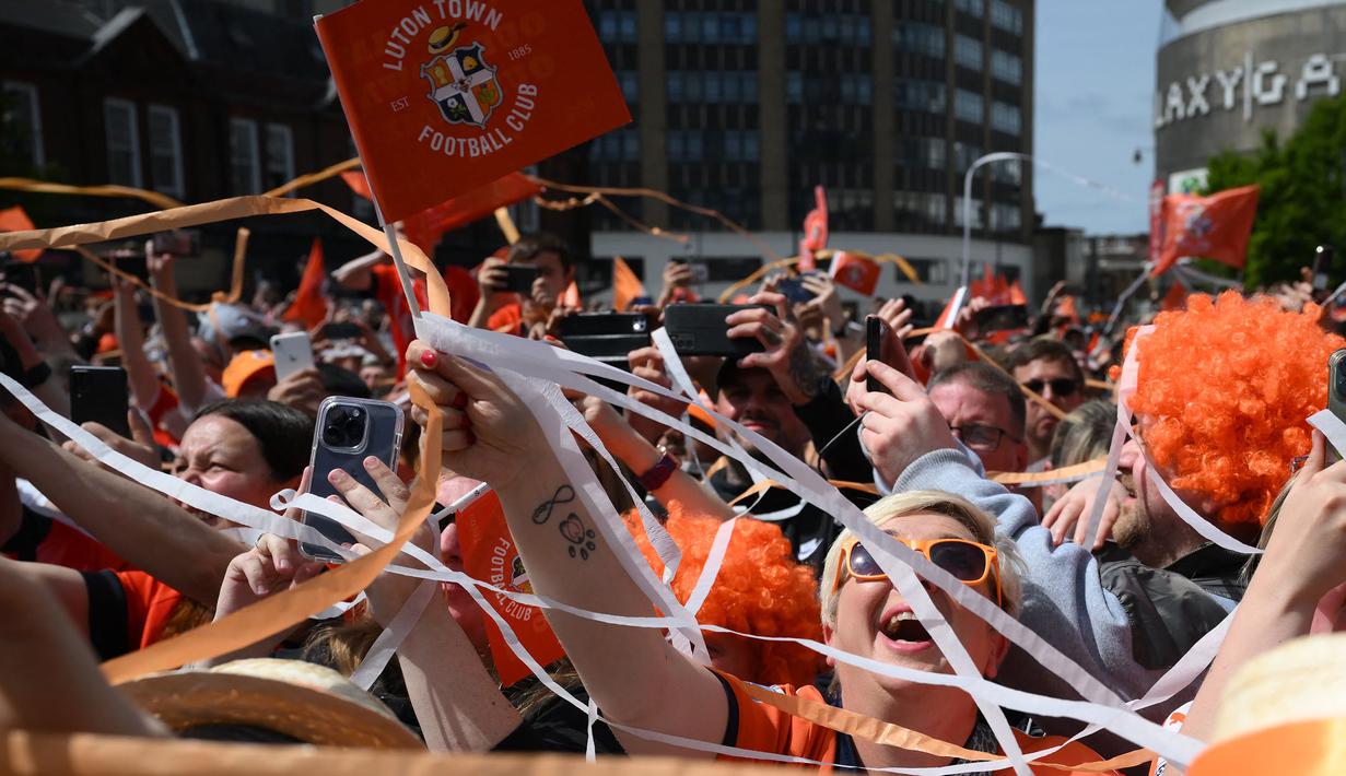 Pendukung Luton Town menyambut kedatangan parade bus timnya melewati jalanan di Luton, Inggris setelah berhasil promosi ke Liga Inggris musim 2023/2024 pada Senin (29/05/2023) waktu setempat. The Hatters sukses menyegel tiket promosi setelah memenangkan laga play-off divisi Championship melawan Covetry City 6-5 melalui adu penalti di Wembley, Sabtu (27/5/2023). (AFP/Daniel Leal)