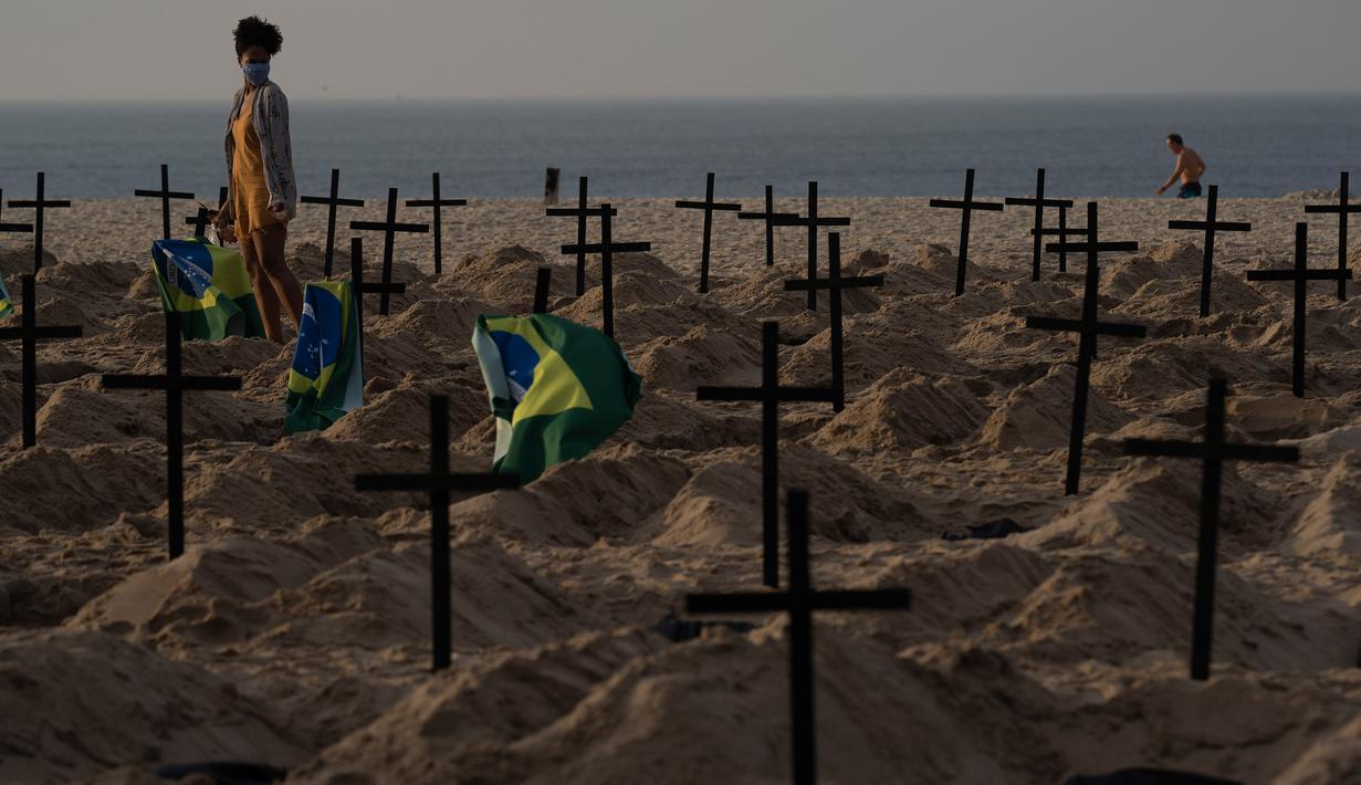 Seorang perempuan berjalan di antara ratusan kuburan di pantai Copacabana, Rio de Janeiro, Kamis (11/6/2020). Aksi simbolis yang dilakukan oleh kelompok LSM Rio de Paz itu sebagai bentuk protes atas respons pemerintah Brasil dalam menangani pandemi Covid-19. (AP Photo/Leo Correa)