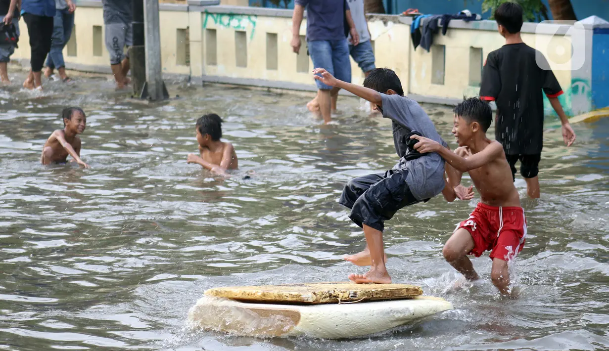 Sejumlah anak-anak bermain di genangan air akibat banjir rob di kawasan pintu masuk Pelabuhan Nizam Zachman, Muara Baru, Jakarta, Jumat (5/6/2020). Banjir rob di Pelabuhan Muara Baru tersebut terjadi akibat cuaca ekstrem serta pasang air laut. (Liputan6.com/Helmi Fithriansyah)
