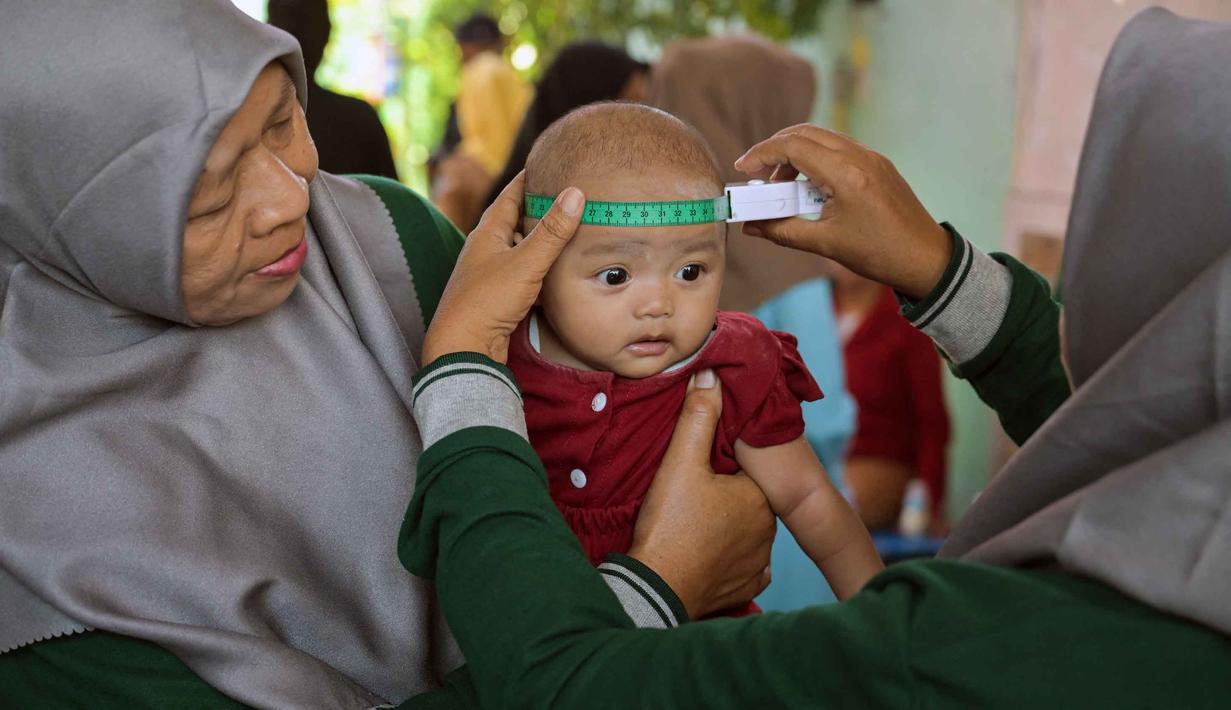 Seorang tenaga kesehatan mengukur lingkar kepala bayi selama program imunisasi massal di Surabaya pada 15 September 2025. (Juni KRISWANTO/AFP)