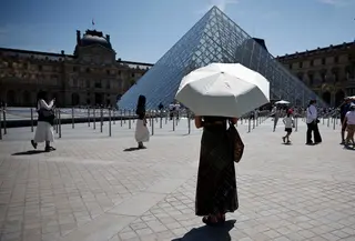 Seseorang berlindung di bawah payung di depan museum Louvre di Paris saat gelombang panas yang memecahkan rekor melanda sebagian besar Eropa Barat pada Kamis 28 Mei 2026. (SIMON WOHLFAHRT/AFP)