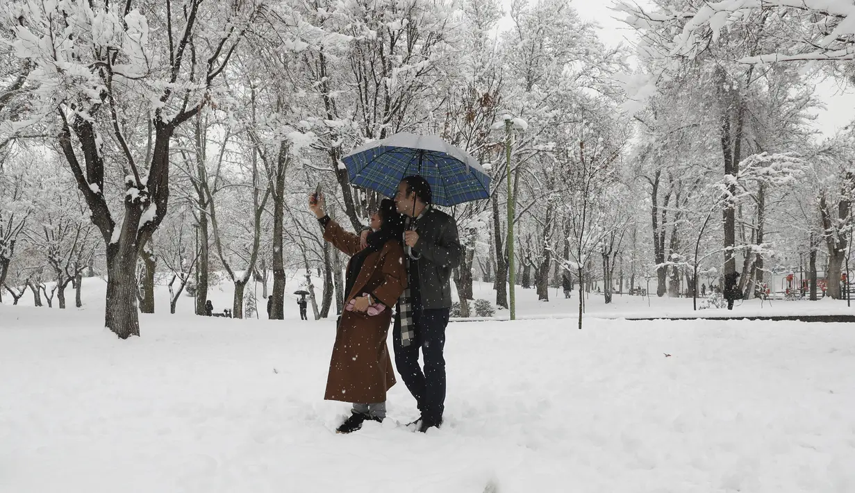 Pasangan berselfie ketika mereka menikmati salju di sebuah taman di Teheran utara, Iran (19/1/2020). Salju tebal menutupi jalan-jalan Teheran, menyebabkan penundaan penerbangan dan munutup sekolah, kata pihak berwenang di ibukota Iran. (AP Photo / Vahid Salemi)