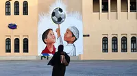 Seorang wanita berjalan melewati mural di Doha, Qatar pada 8 November 2022, menjelang turnamen sepak bola Piala Dunia 2022. (Gabriel BOUYS/AFP)