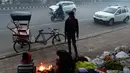 Para tunawisma menghangatkan diri dengan api kecil di pagi berkabut dingin di New Delhi (25/12). India ditetapkan darurat polusi udara. Kualitas udara yang semakin buruk dan kabut beracun menyelimuti. (AFP Photo/Prakash Singh)