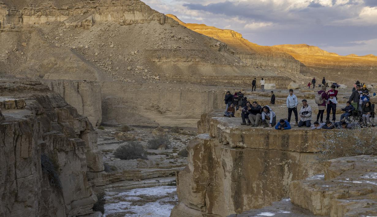 Warga Israel menyaksikan banjir bandang terjadi menyusul hujan lebat di gurun Negev di sebelah timur kota Dimona Israel pada 26 Desember 2022. Hujan lebat mengguyur Israel pada hari Senin (26/12) membanjiri jalan-jalan kota, memicu banjir bandang di dasar sungai gurun yang kering dan membasahi daerah pedesaan karena suhu turun ke level terendah musim ini. (AFP/Menahem Kahana)