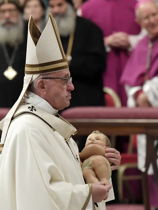 Paus Fransiskus membawa patung bayi Yesus selama memimpin misa Natal di Basilika Santo Petrus, Vatikan, (24/12). Ini merupakan Natal keenam bagi pria berusia 82 tahun ini sebagai kepala Gereja Katolik Roma. (AFP Photo/Tiziana Fabi)