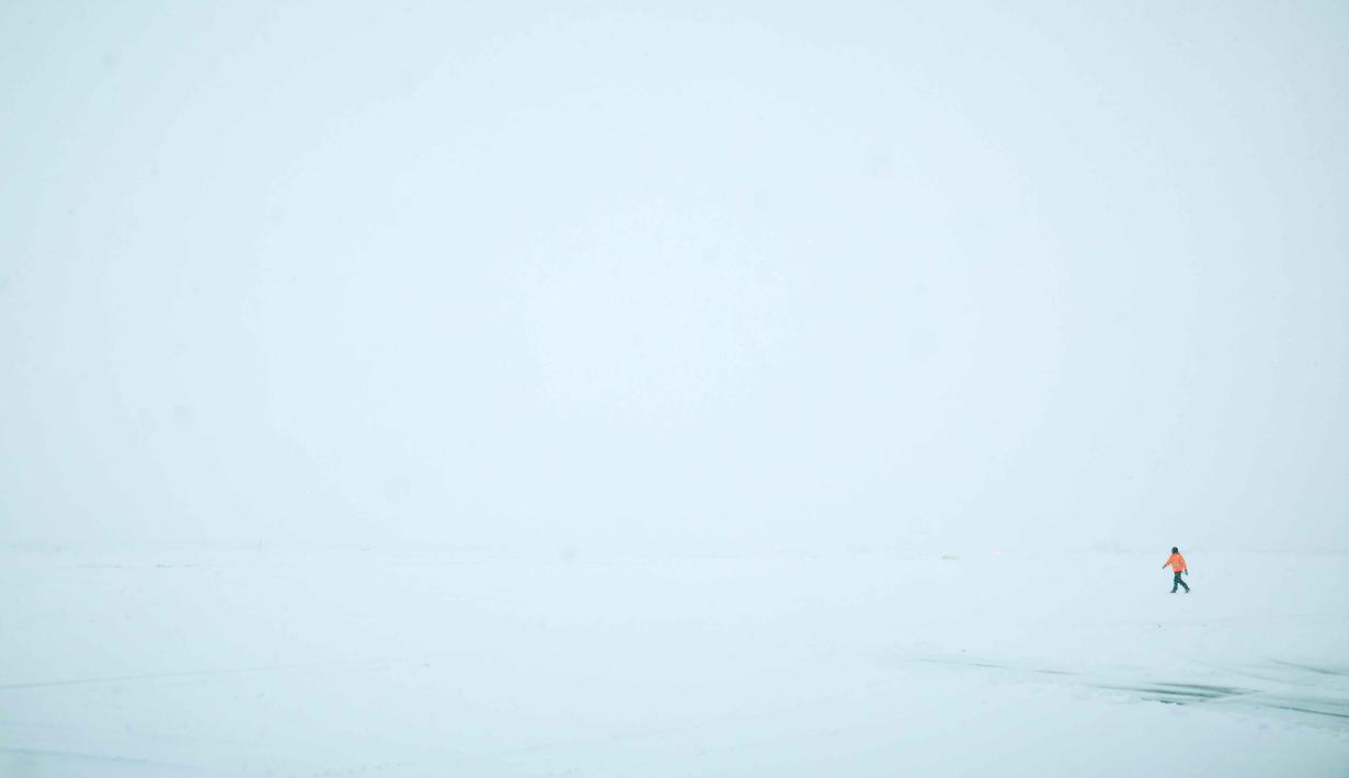 Langkah serupa juga diambil oleh Bandara Orly yang membatalkan seperempat jadwal penerbangannya. Tampak foto yang menunjukkan seorang karyawan berjalan di atas salju di dekat landasan pacu selama hujan salju lebat, yang menyebabkan pembatalan penerbangan di Bandara Orly, selatan Paris pada 7 Januari 2026. (Kiran RIDLEY/AFP)