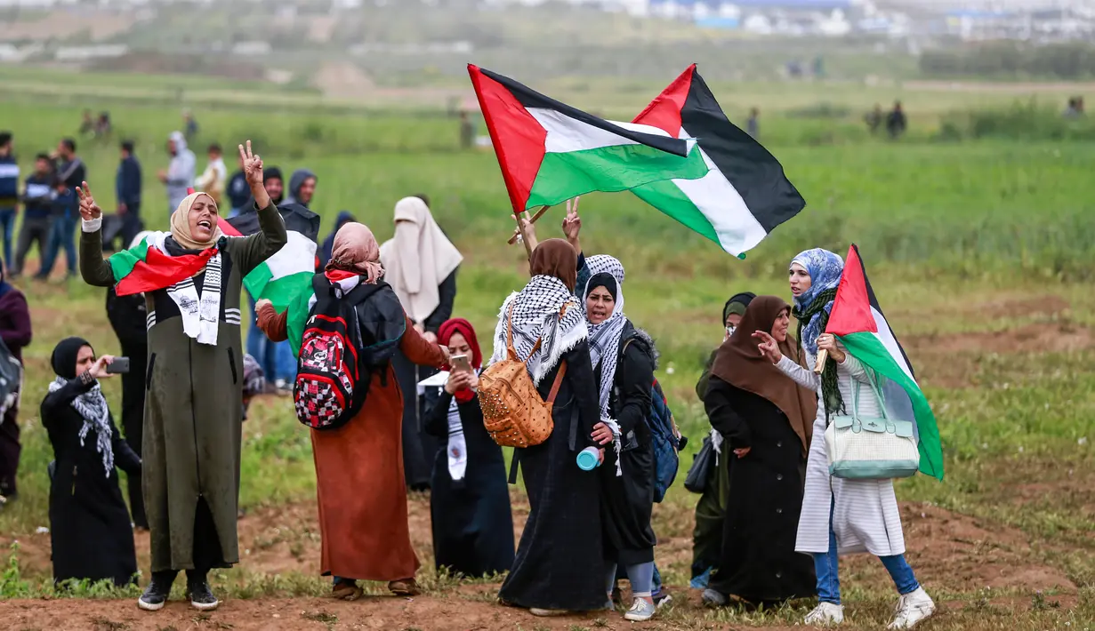 Para wanita mengibarkan bendera Palestina selama bentrokan dengan tentara Israel dalam demonstrasi untuk memperingati Hari Tanah di Tepi Barat, Sabtu (30/3). (Photo by ANAS BABA/AFP)