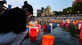 Foto yang diambil pada tanggal 6 Agustus 2024 ini menunjukkan seorang wanita yang sedang berdoa saat lentera dilepaskan ke Sungai Motoyasu, di seberang Kubah Bom Atom dekat Taman Peringatan Perdamaian di Hiroshima. (JIJI Press/AFP/Japan OUT)