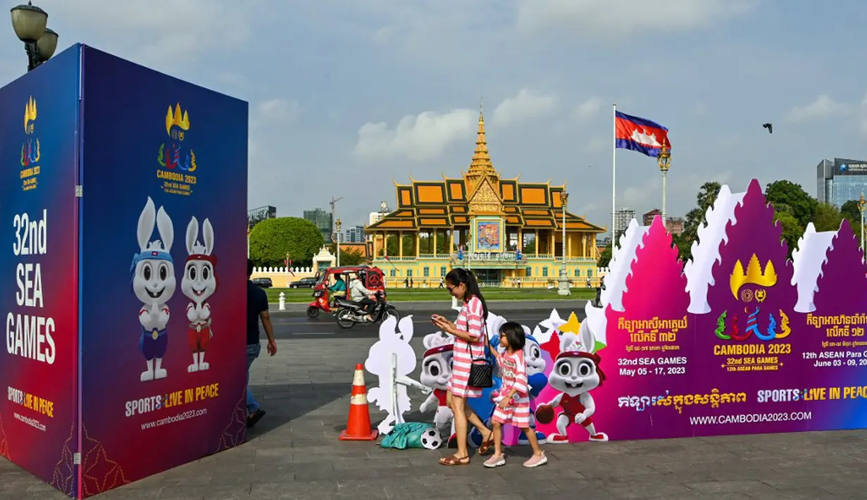 <p>Seorang wanita dan putrinya berjalan di samping tanda menjelang upacara pembukaan Pesta Olahraga Asia Tenggara (SEA Games) ke-32 di Phnom Penh, Kamboja, Kamis (4/5/2023). (TANG CHHIN Sothy/AFP)</p>