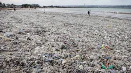 Volume sampah kiriman mencapai puluhan ton per hari, yang didominasi oleh limbah plastik dan potongan kayu. Tampak dalam foto, para pekerja dan warga membersihkan ceceran dan tumpukan sampah plastik yang terdampar di Pantai Jimbaran, Bali, pada Selasa 10 Maret 2026. (Lana Priatna/AFP)