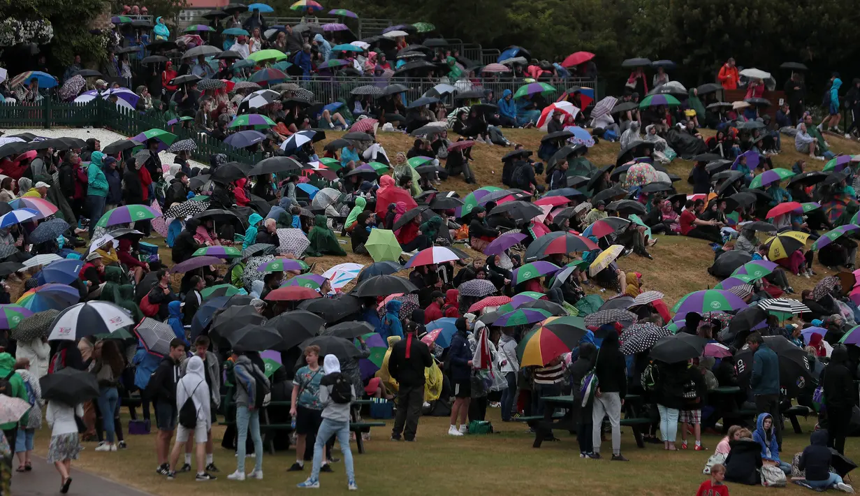 Para penonton memakai payung saat mereka menyaksikan kejuaraan tenis Wimbledon 2017 di The All England Lawn Tennis Club, London (11/7). Walaupun Hujan, Para penonton tetap antusias untuk menyaksikan idolanya bertanding . (AFP Photo/Daniel Leal Olivas)