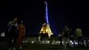 <p>Orang-orang berjalan di dekat Menara Eiffel di Paris yang diterangi dengan warna bendera nasional Ukraina, pada 9 Mei 2022. Memperingati Hari Eropa, Menara Eiffel memproyeksikan bendera Ukraina sebagai solidaritas untuk rakyat Ukraina di tengah invasi Rusia. (Ludovic MARIN / AFP)</p>