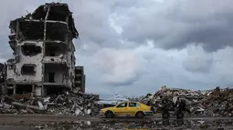 Di sisi lain, Perserikatan Bangsa Bangsa (PBB) memperkirakan, sejak konflik antara Israel dan Hamas dimulai pada Oktober 2023 lalu, sekitar 92 persen dari seluruh bangunan tempat tinggal di Gaza telah rusak atau hancur. Tampak dalam foto, seorang pria mengendarai mobil kuning di samping genangan air di lingkungan Al-Saftawi, sebelah barat kota Jabalia di Jalur Gaza utara pada Rabu 10 Desember 2025. (BASHAR TALEB/AFP)