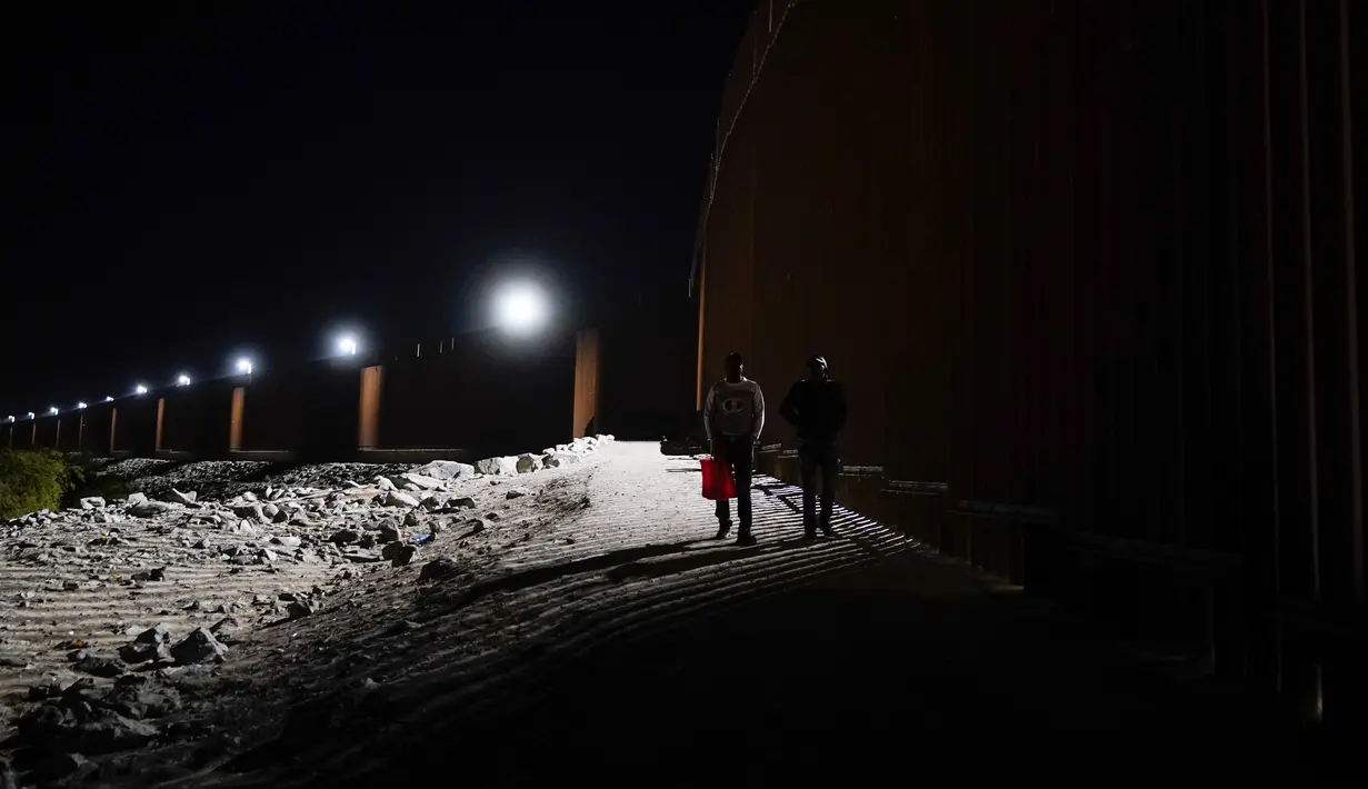 Dua pria dari Kuba mendekati tembok perbatasan dari Meksiko sebelum menyerah kepada pihak berwenang untuk mengajukan suaka di dekat Yuma, Arizona, Amerika Serikat, 3 November 2022. Meski tercatat rekor masuknya imigran di perbatasan Amerika Serikat-Meksiko dan kekurangan pekerja di Amerika Serikat, para ahli percaya kebijakan imigrasi Amerika Serikat akan tidak berubah setelah pemilu paruh waktu nanti. (AP Photo/Gregory Bull)