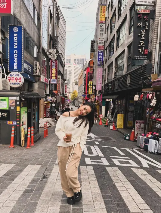 Lihat gaya Fuji pakai atasan knitted putih dengan bahu asimetris, yang memiliki tali kecil sebagai belt di pinggang, dipadukannya dengan celana kargo cokelat, dan sepatu hitam. [Foto: Instagram/fuji_an]