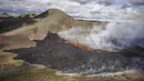 Uap naik dan lava mengalir dari gunung berapi Fagradalsfjall di Islandia pada Rabu (3/8/2022), yang terletak 32 kilometer (20 mil) barat daya ibu kota Reykjavik dan dekat dengan Bandara Internasional Keflavik. Kode merah diumumkan  untuk melarang pesawat terbang di atas lokasi langsung meskipun helikopter akan dikirim untuk mengamati situasi. (AP Photo/Marco Di Marco)