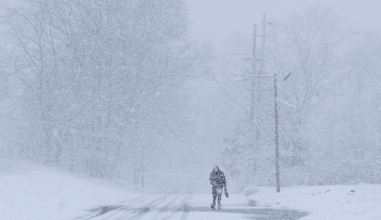 Seorang pria berjalan di bawah salju lebat saat terjadi badai salju di Manville, New Jersey (21/3). Salju tebal yang menutup jalanan ini berpotensi membahayakan warganya. (AP/Julio Cortez)