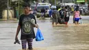 Warga berusaha menyeberangi banjir setelah hujan lebat di Kota Candaba, Filipina (17/12). Ratusan orang mengungsi di atap rumah mereka akibat banjir yang disebabkan topan beberapa hari lalu. (REUTERS/Romeo Ranoco)