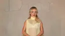 Sabrina Carpenter tampil mengenakan long dress butter yellow berbahan tulle transparan kerah tinggi. Dress sleeveless tersebut semakin menarik dengan aksen bunga 3D besar di bagian rok. Melengkapi tampilannya dengan membawa tas Dior warna senada. [Dok. DIOR]