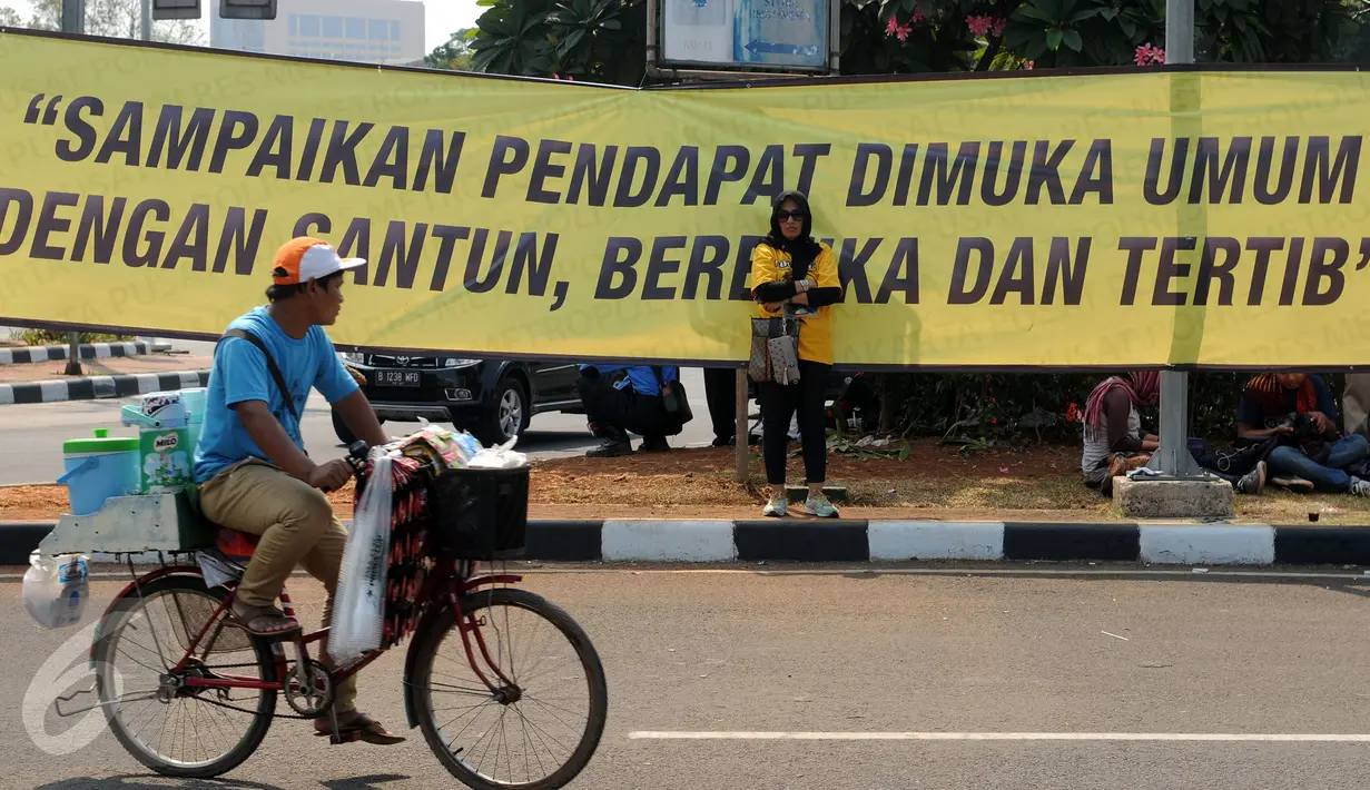 Seorang pedagang melintas di depan spanduk di pertigaan Medan Merdeka Selatan dan Barat saat ribuan buruh dari berbagai elemen organisasi melakukan aksi di depan Istana Negara, Jakarta, Selasa (1/9/2015). (Liputan6.com/Helmi Fithriansyah)