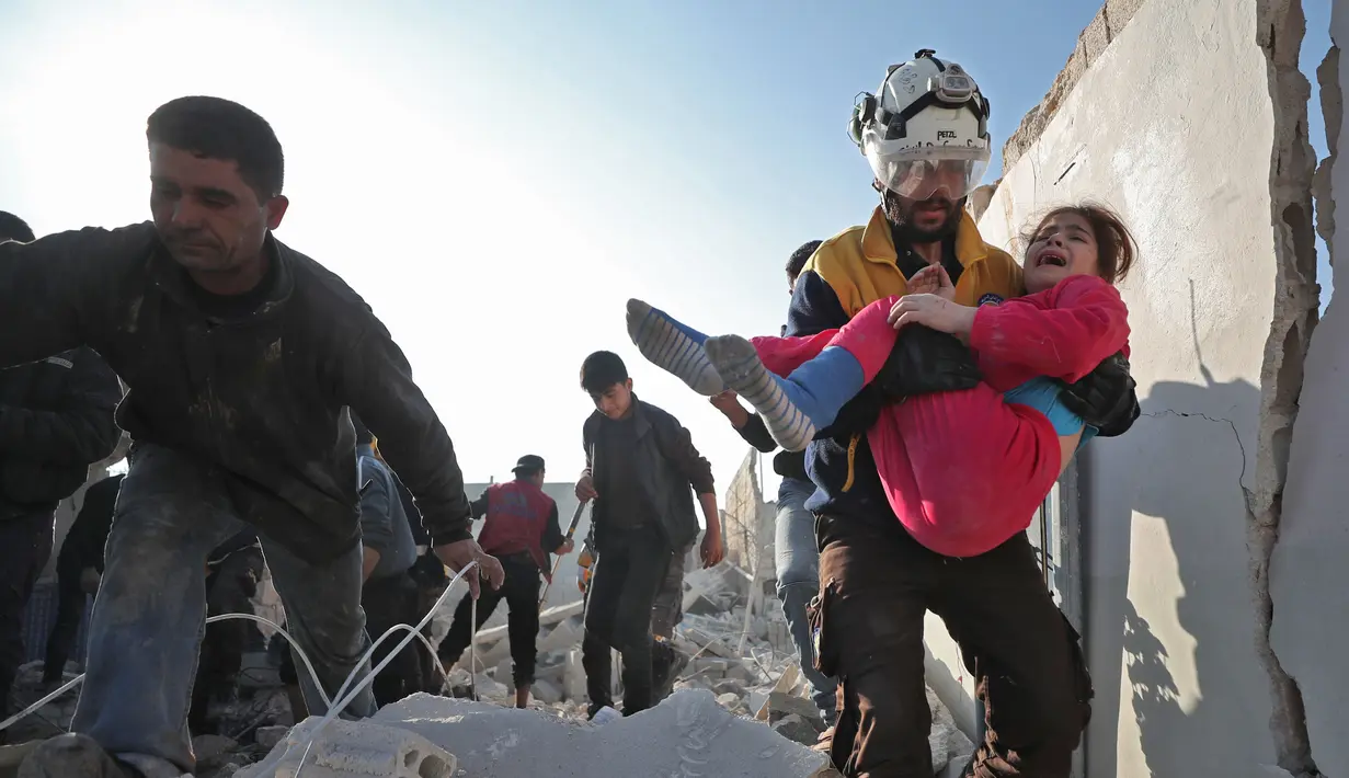 Anggota Syrian Civil Defence atau White Helmets membawa seorang gadis yang diselamatkan dari timbunan puing bangunan usai serangan udara pasukan pemerintah di Desa Tal Mardikh, Provinsi Idlib, Suriah, Kamis (19/12/2019). Pasukan Suriah kian intens menyerang Idlib. (Omar HAJ KADOUR/AFP)
