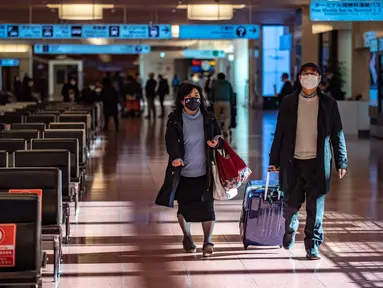 Penumpang berjalan melalui aula kedatangan di Bandara Internasional Haneda Tokyo, Jumat (18/2/2022). Pemerintah Jepang mengumumkan rencana untuk melonggarkan aturan perbatasan virus bagi pekerja dan pelajar. (AFP/Philip Fong)