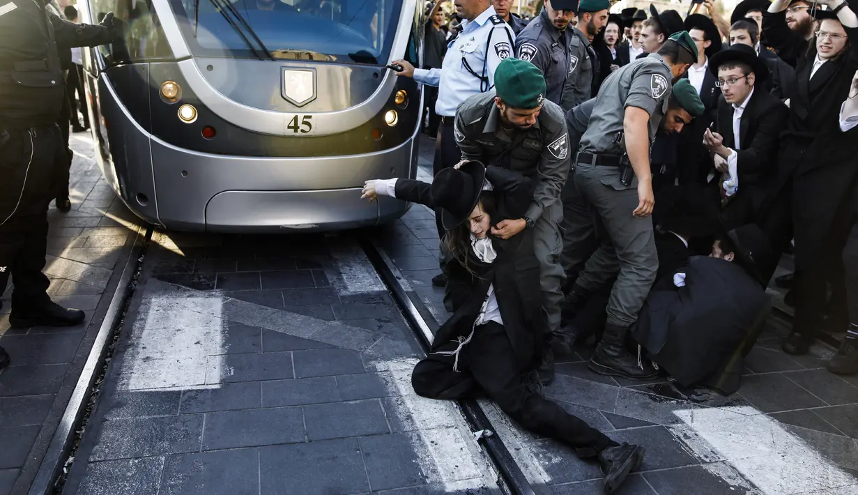 Pasukan keamanan Israel saling tarik-menarik dengan demonstran Yahudi Ultra-Ortodoks yang memblokir jalan utama saat melakukan aksi menentang wajib militer Israel di Yerusalem (17/10). (AFP Photo/Menahem Kahana)
