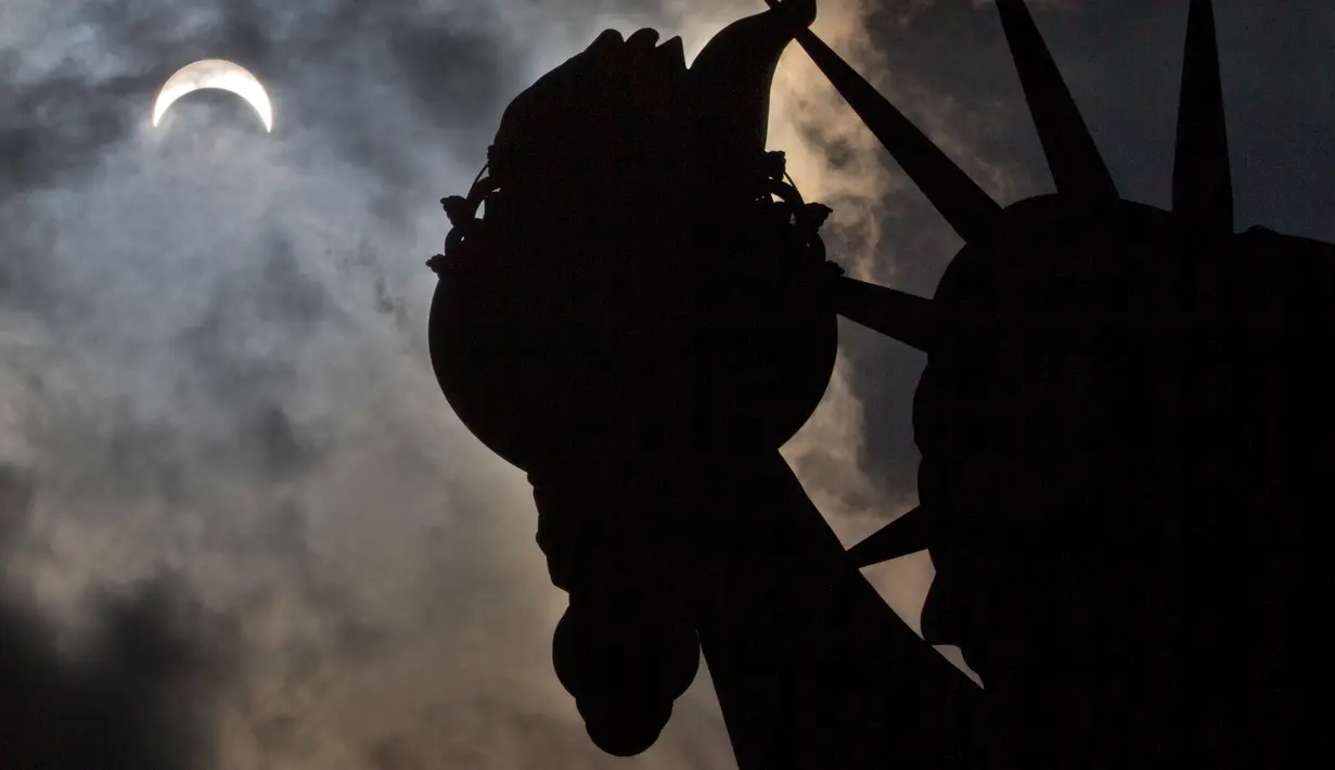 Gerhana matahari parsial terlihat di atas Patung Liberty, New York, Senin (21/8). Gerhana Matahari Total tahun ini membuat gelap sebagian wilayah Amerika Serikat yang dilintasi oleh bayangan Bulan. (AP Photo/Seth Wenig)