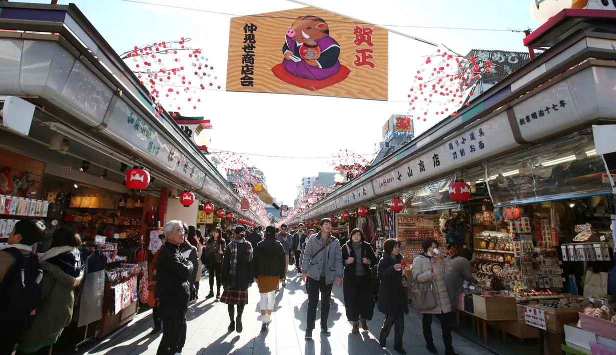 Pejalan kaki melintas di bawah dekorasi shio babi tanah yang mengarah ke kuil Buddha Asakusa Sensoji di Tokyo, Jepang, Kamis (27/12). Babi dipercaya memiliki sifatnya enerjik namun berhati-hati dalam mengambil keputusa. (AP Photo/Koji Sasahara)