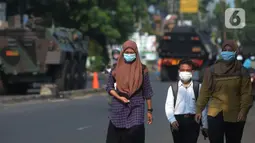 Warga berjalan dengan latar belakang kendaraan taktis jenis barracuda dan panser yang disiagakan di pos penyekatan di Jalan Raya Bogor, Jakarta, Selasa (6/7/2021). Petugas Gabungan Polri dan TNI menyiapkan kendaraan taktis untuk membantu penyekatan selama PPKM Darurat. (merdeka.com/Imam Buhori)