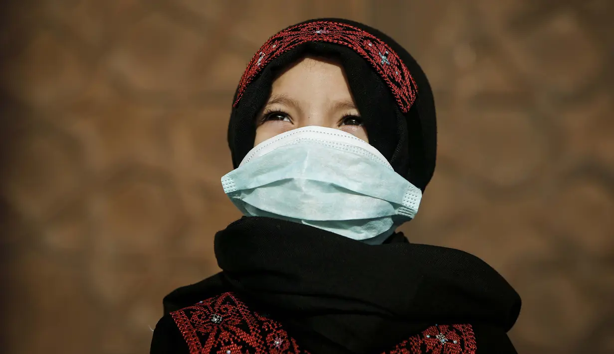 Seorang anak Palestina yang mengenakan masker karena pandemi Covid-19 berdiri di luar sebuah masjid untuk mengikuti salat Idul Fitri di Kota Gaza pada 24 Mei 2020. (Photo by MOHAMMED ABED / AFP)