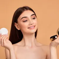 Seorang perempuan sedang bercermin sambil memegang puff make up (Foto Dok: Freepik/erstudio).