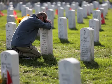Chris Plank memegang nisan temannya Sersan Mayor Bradly Dean Conner saat peringatan Hari Veteran di Pemakaman Nasional Arlington, AS, Senin (11/11/2019). Rakyat AS memperingati Hari Veteran untuk menghormati mereka yang pernah bertugas di militer AS. (Alex Wong/Getty Images/AFP)