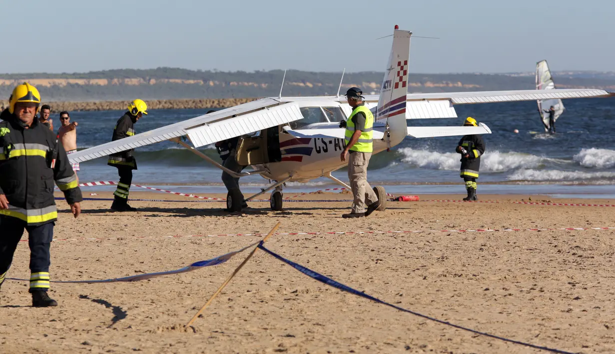 Petugas pemadam berdiri di samping sebuah pesawat kecil yang mendarat darurat di pantai Sao Joao yang ramai dekat Lisbon, Portugal, Rabu (2/8). Pesawat kecil yang diketahui jenis cessna itu membawa dua orang termasuk pilot. (AP Photo/Armando Franca)