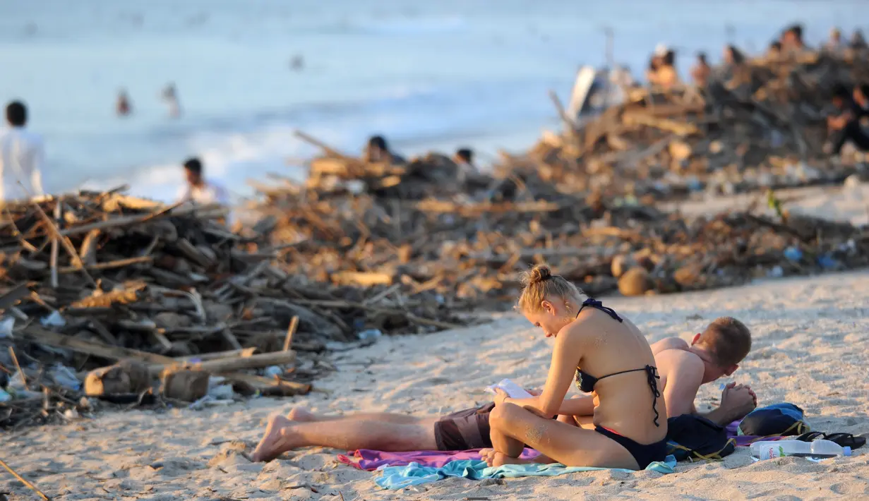 Turis asing bersantai dekat sampah yang terdampar akibat cuaca buruk di Pantai Kuta, Bali, Jumat (15/2). Hujan deras disertai angin kencang yang melanda Bali berdampak pada arus laut yang terus membawa sampah dari daerah lain. (SONNY TUMBELAKA/AFP)