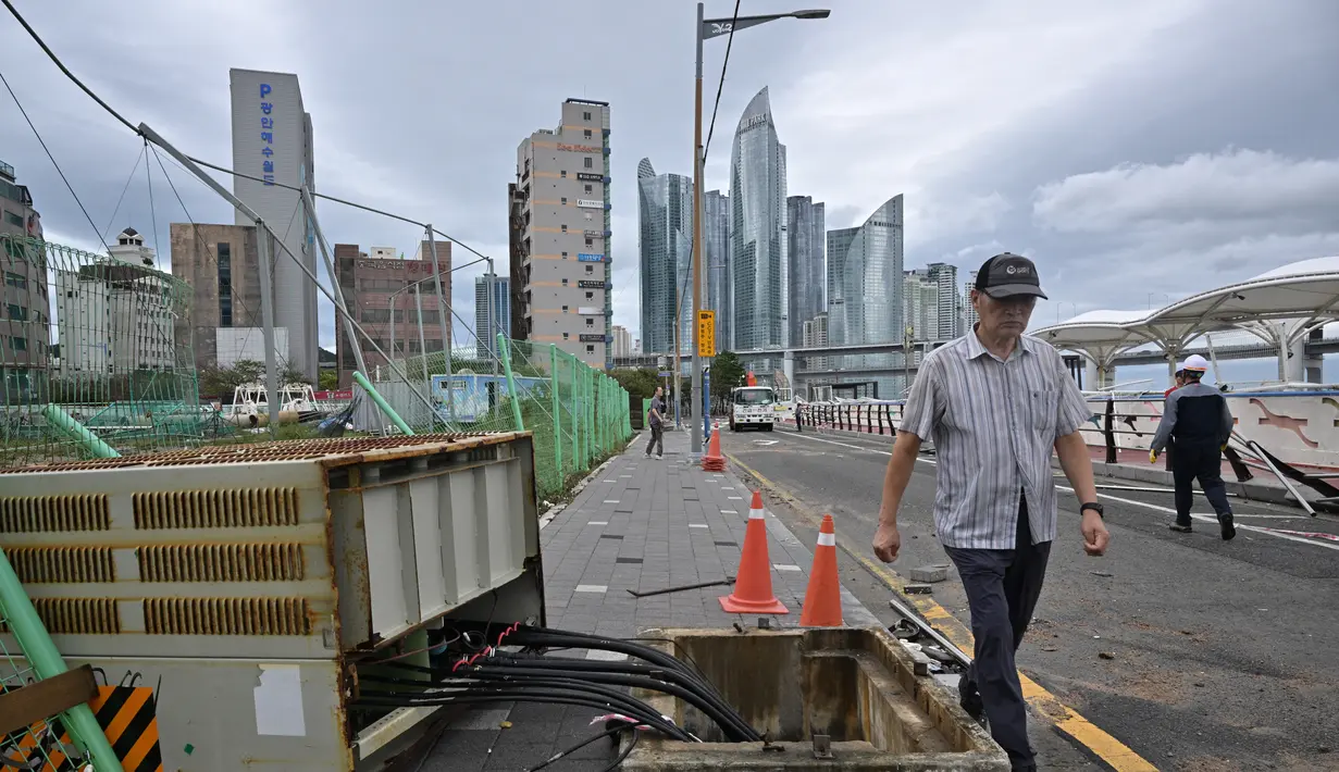 Seorang pria berjalan melewati kotak kontrol listrik yang rusak di jalan, setelah Topan Hinnamnor melewati Busan, Korea Selatan (6/9/2022). (AFP/Anthony Wallace)