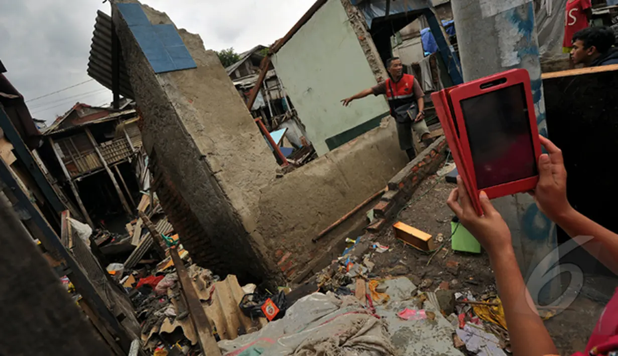 Seorang warga saat mengambil gambar rumah yang rubuh dikawasan muara baru, Jakarta, Jumat (13/2/2015).  Sebanyak 33 rumah di muara baru Jakarta Utara mengalami kemiringan parah dan 2 buah rumah ambruk akibat banjir. (Liputan6.com/Faizal Fanani)