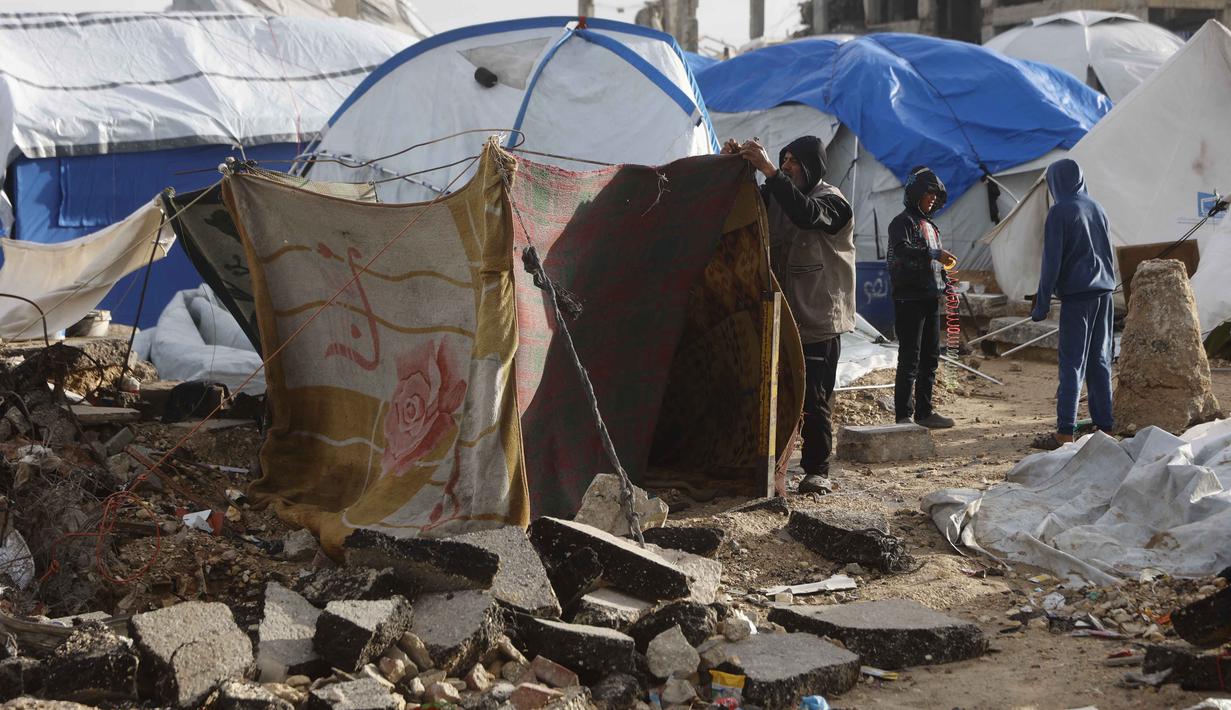 Dan kini tenda-tenda tersebut terpapar langsung massa udara kutub yang membawa suhu dingin ekstrem. Tampak dalam foto, seorang pria Palestina yang mengungsi memperbaiki tenda yang didirikan di sepanjang pantai Kota Gaza saat angin musim dingin yang kencang menerpa wilayah tersebut pada Selasa 13 Januari 2026. (Omar AL-QATTAA/AFP)