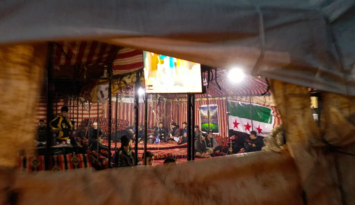 Para pengungsi Suriah menonton pertandingan antara Maroko dan Portugal selama turnamen Piala Dunia Qatar 2022 di dalam tenda di kamp Barisha di bagian utara provinsi Idlib (10/12/2022). Acara nonton bareng ini diselenggarakan oleh sukarelawan organisasi kemanusiaan untuk para penggemar. (AFP/Omar Haj Kadour)