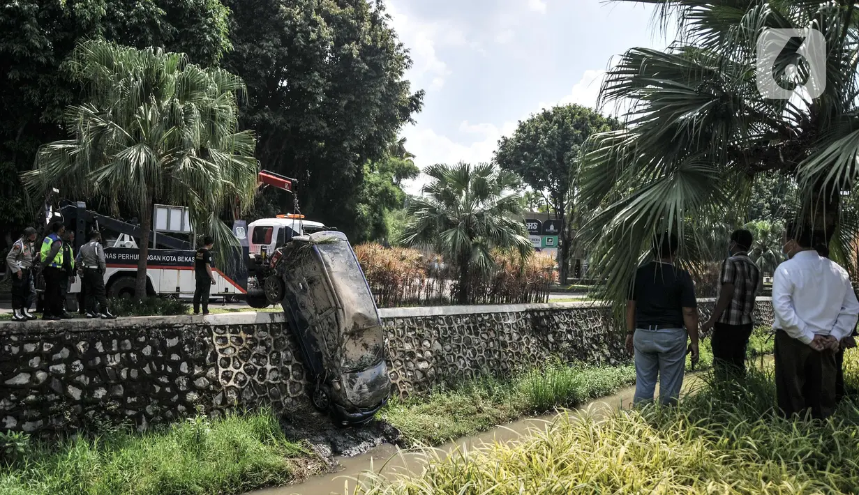 Warga saat menyaksikan petugas melakukan evakuasi sebuah mobil yang terperosok ke kali di kawasan Harapan Indah, Bekasi, Jawa Barat, Rabu (16/2/2022). Beruntung tidak ada korban jiwa dalam kejadian tersebut, namun mobil mengalami rusak parah. (merdeka.com/Iqbal S. Nugroho)