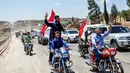 Pengendara motor mengibarkan bendera Suriah saat melintasi jalan raya utama antara Homs dan Hama yang dibuka kembali, Rabu (6/6). Pemerintah Suriah membuka kembali jalan raya Homs-Hama setelah ditutup selama hampir tujuh tahun. (AFP/STRINGER)
