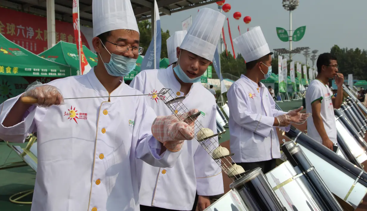 Para koki memasak roti menggunakan tabung logam dan kaca yang dipanaskan oleh cermin melengkung untuk menangkap sinar matahari di Dezhou, Shandong Timur, Cina, 2 Agustus 2018. Koki memasak dengan kompor tenaga surya. (AP Foto/Fu Ting)