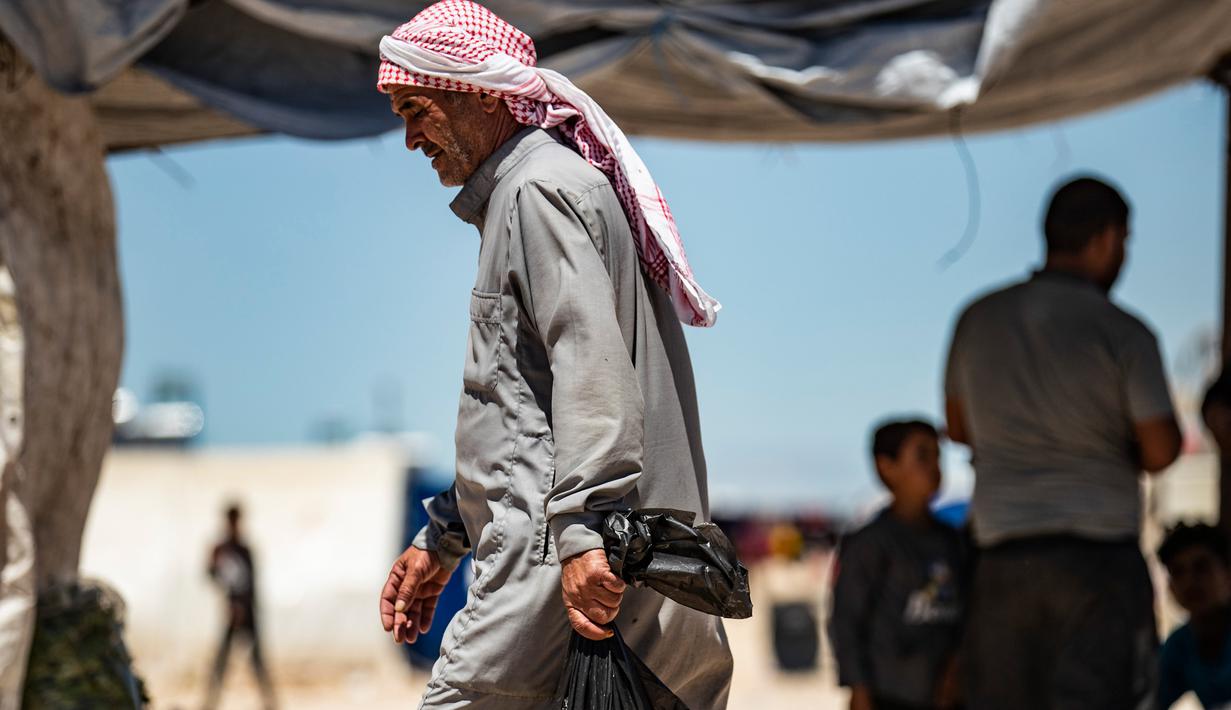 Seorang pria Suriah yang terlantar membawa seekor ayam dalam sebuah tas kembali ke tendanya belanjaan selama bulan suci Ramadan di kamp Washukanni untuk para pengungsi internal di provinsi Hasakeh di timur laut Suriah, (10/5/2020). (AFP/Delil Souleiman)