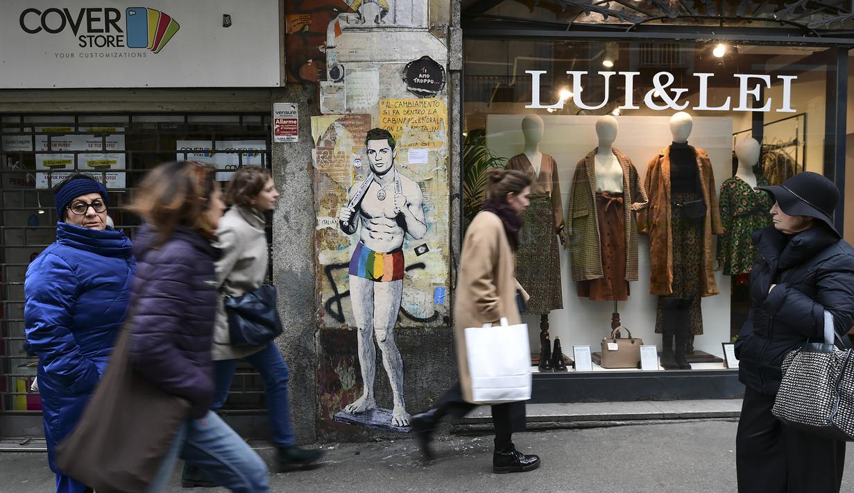 Sejumlah warga melintasi mural dengan gambar bintang Juventus, Cristiano Ronaldo, yang terdapat di Milan, Senin (19/3). Mural berjudul Cristiano's Secret ini karya seniman Italia, TvBoy. (AFP/Miguel Medina)
